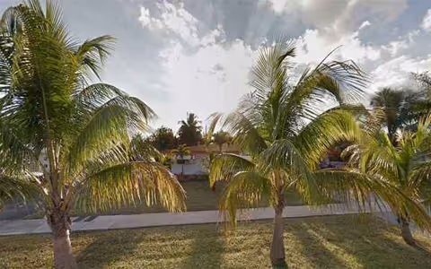 Palm trees line a grassy area in front of a retirement home under a cloudy sky.