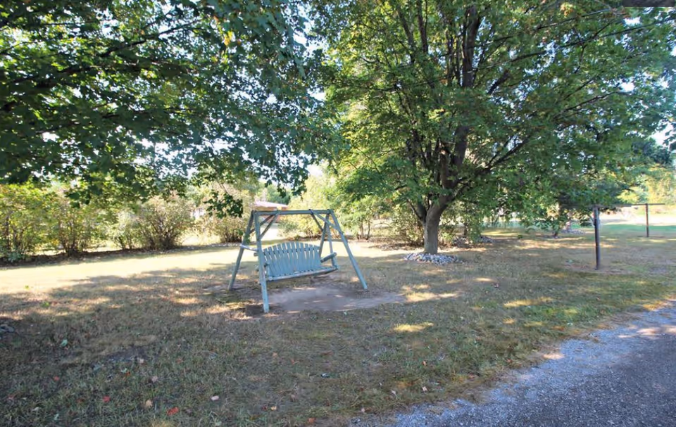 A painted wooden swing bench beneath large trees in a grassy yard.