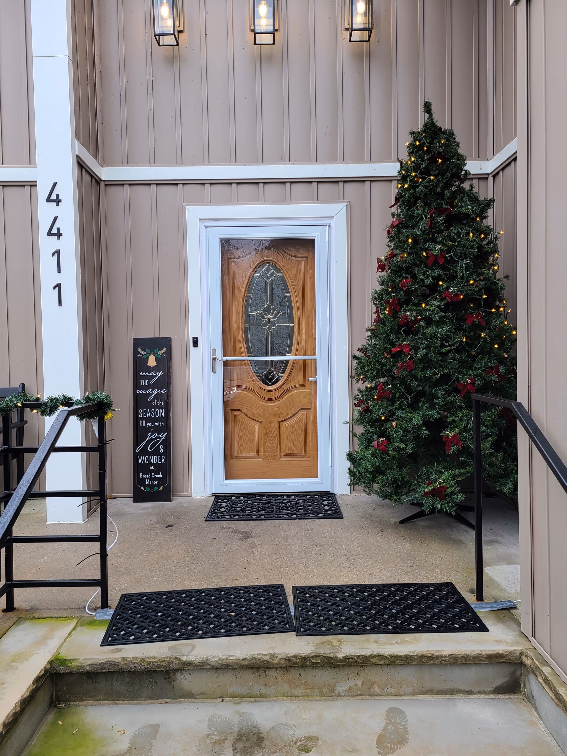 Front entrance with a wooden door, holiday-decorated Christmas tree, and house number 4411 on the porch.