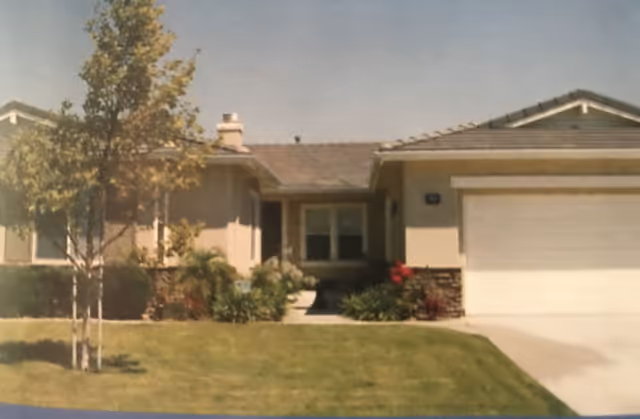 Single-story house with a garage, front lawn, small trees and shrubs, and a paved walkway to the entrance.