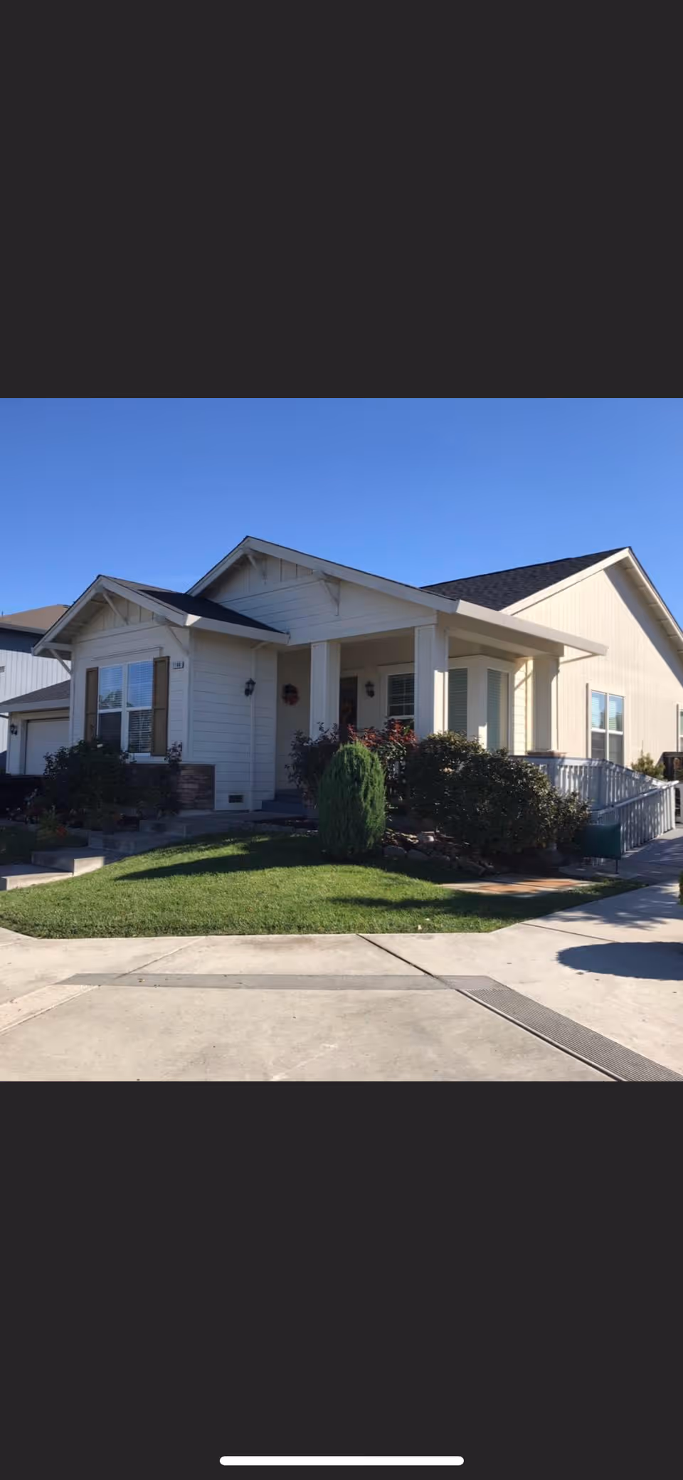Single-story beige house with a covered front porch, landscaped lawn, and driveway under a clear blue sky.
