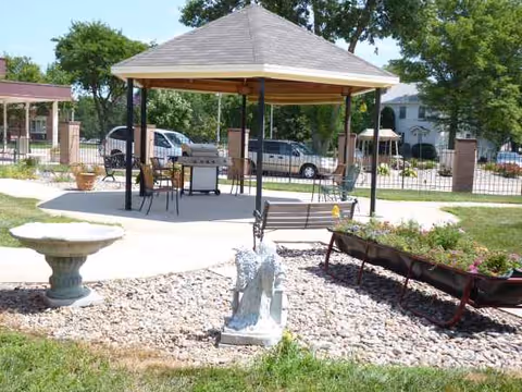 Outdoor courtyard at Blue Valley Lutheran Homes featuring a gazebo, benches, statue, and garden beds.