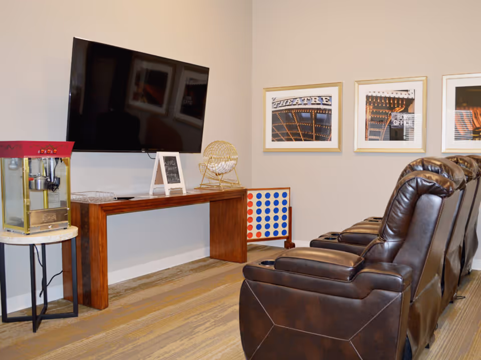 Small movie lounge with leather recliners facing a wall-mounted TV, a popcorn machine, and framed pictures on the wall.