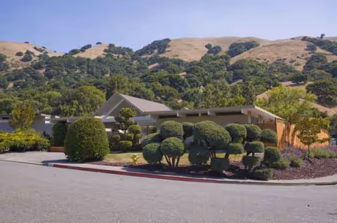 Front view of Lucas Valley Lodge with manicured shrubs and hillside backdrop.