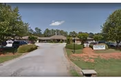 Driveway leading to a single-story assisted living building with landscaping and a freestanding sign at the entrance.