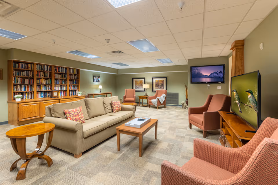 Comfortable communal lounge with a sofa, armchairs, bookshelves, and two televisions.