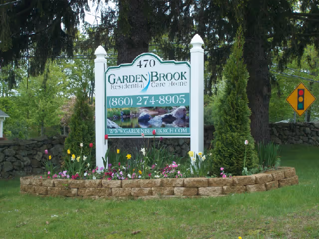 A landscaped roadside sign for Garden Brook Residential Care Home surrounded by flowers and trees.