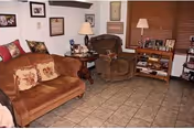 Cozy living room with a sofa, armchair, side tables, lamps, bookshelf and framed pictures on tiled floor.