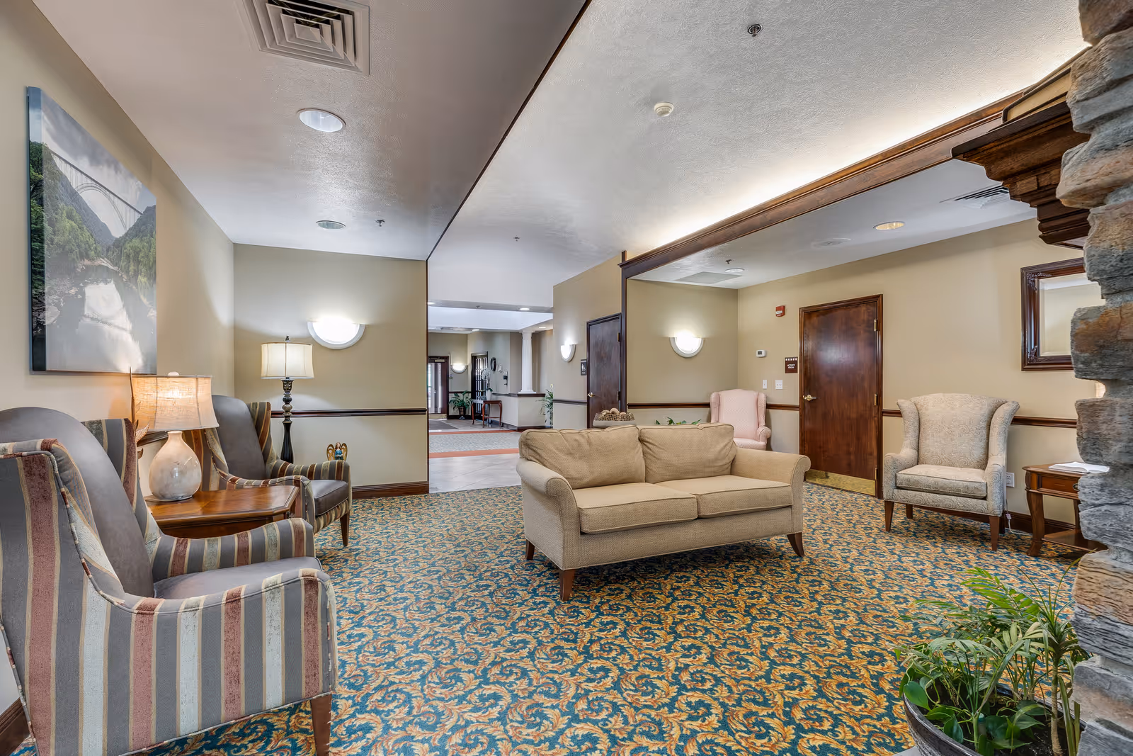 Seating area in a senior living facility lobby with a sofa, armchairs, side tables, lamps and patterned carpet.