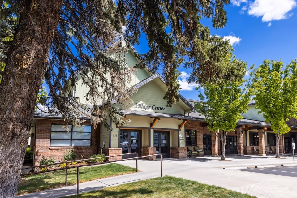 Front exterior of the Village Center at The Terraces at Summitview showing the entrance, brick façade, trees, and a sidewalk ramp.