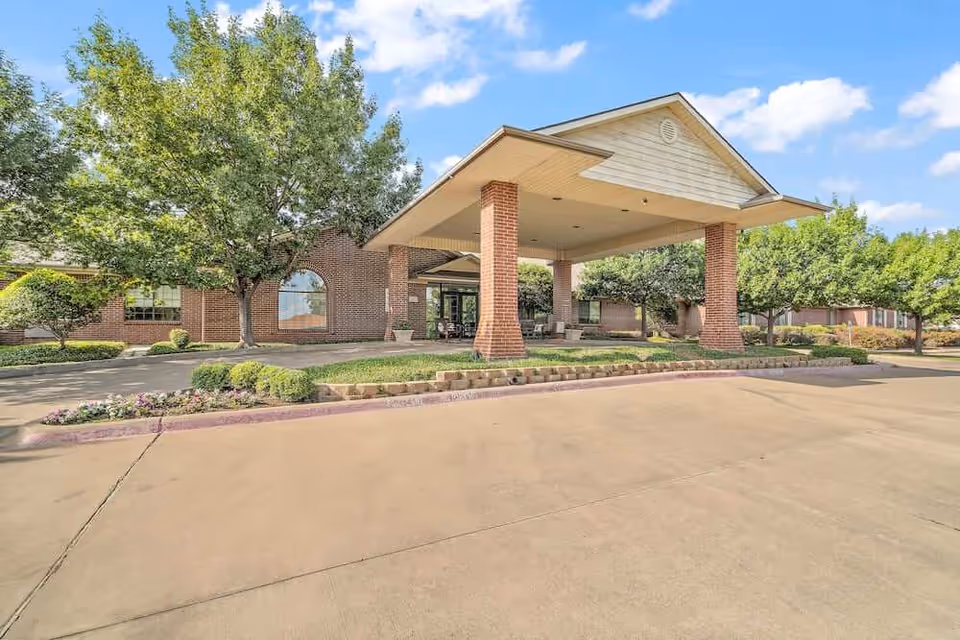 Front exterior view of Morada North Richland Hills facility showing a covered entrance with brick pillars, surrounded by trees and landscaping under a partly cloudy sky.