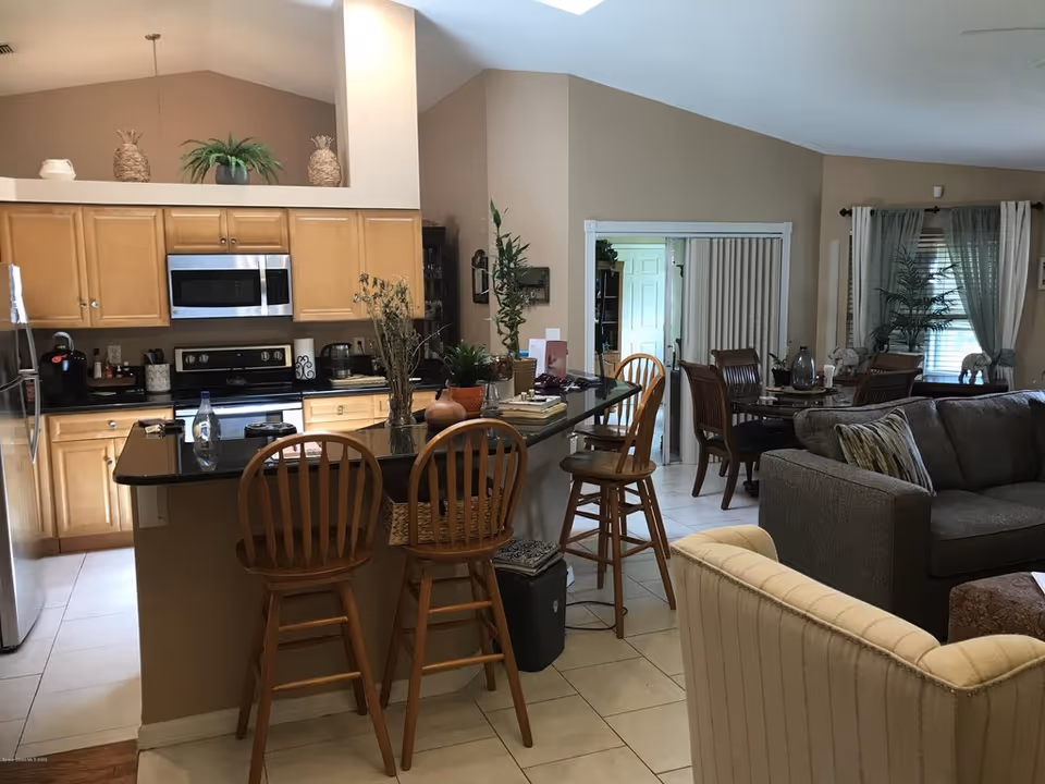 Open-plan kitchen and living area with a granite-topped island, wooden bar stools, and adjacent dining and seating areas.