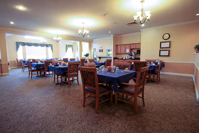 Spacious dining room with multiple tables set with blue tablecloths and wooden chairs under chandeliers.