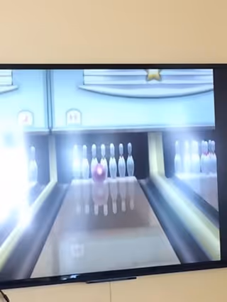 A television screen displaying a virtual bowling game with pins set up at the end of a lane and a bowling ball approaching them.