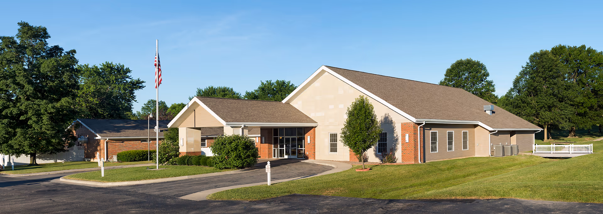 Single-story building front with an entrance canopy, an American flag, and a manicured lawn under a clear sky.