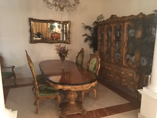 Ornate dining room with a carved wooden table, green upholstered chairs, a matching china cabinet, wall mirror, and chandelier.