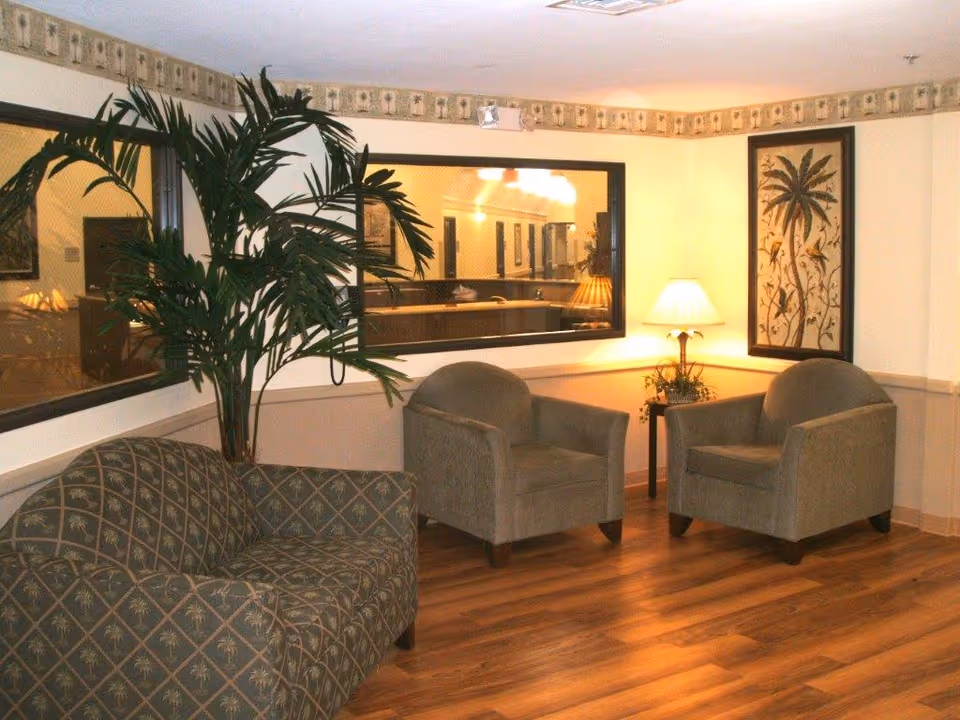 Small seating area with two armchairs, a patterned sofa, a potted plant, a table lamp, and framed artwork on a wood floor.