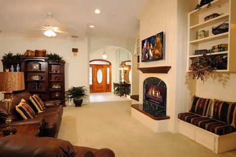 Spacious living room featuring leather seating, a wall-mounted TV above a fireplace, built-in shelving, and an arched entryway.
