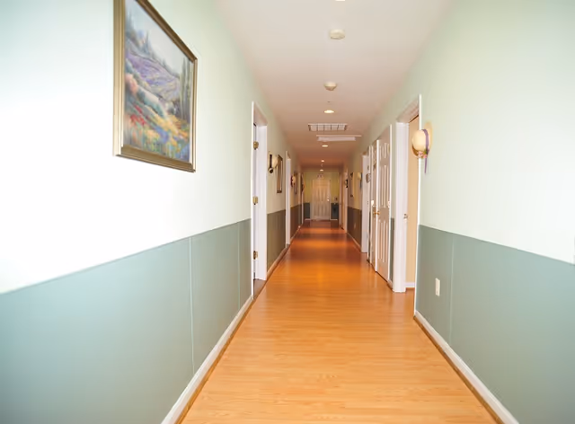Long, well-lit interior hallway with wood flooring, doors on both sides and framed artwork on the wall.