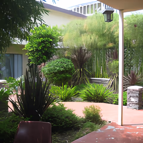 Covered patio overlooking a lush courtyard garden with assorted shrubs, tall grasses and a small stone fountain.