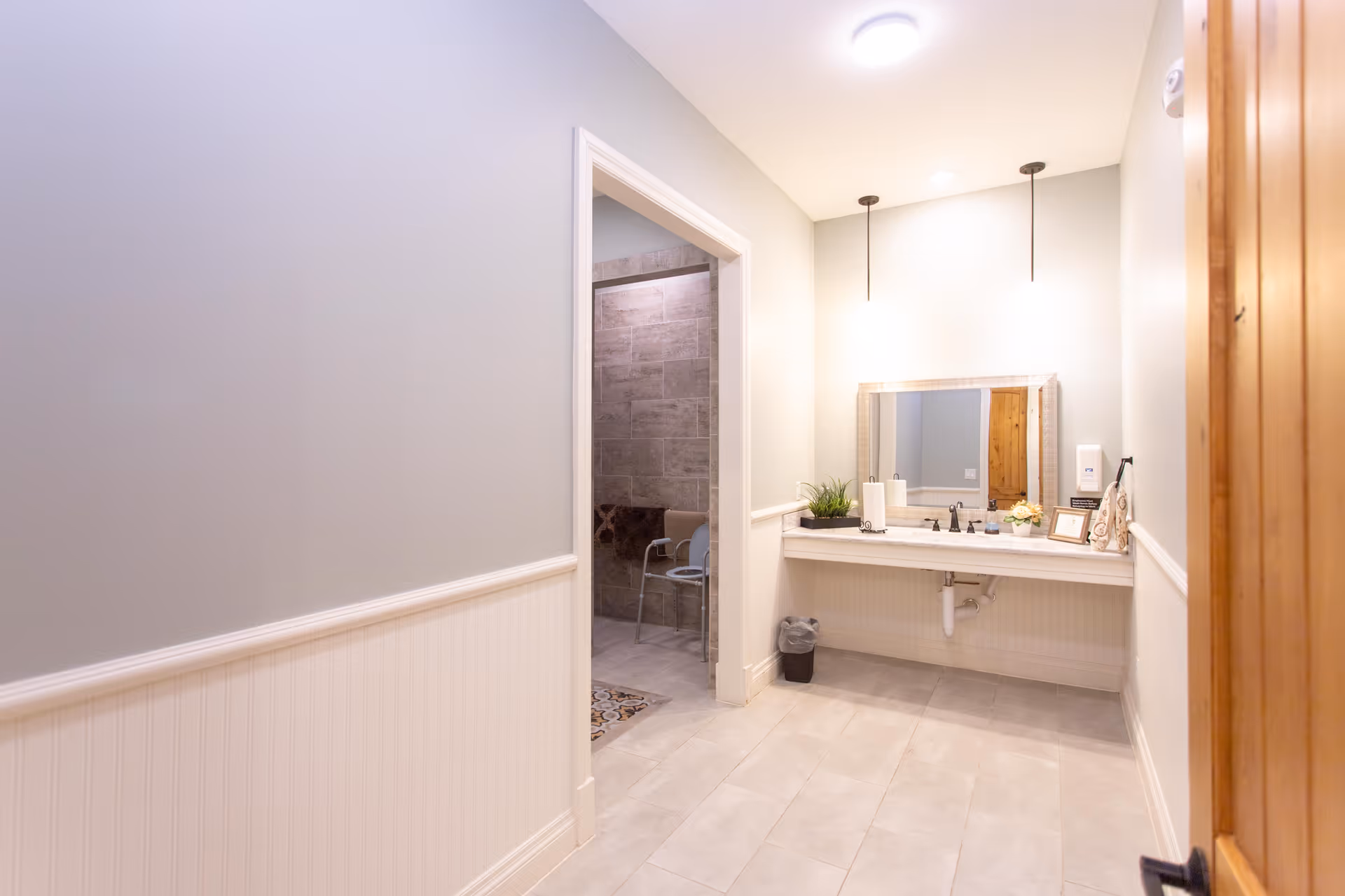 Well-lit accessible bathroom vanity with a mirror and sink, and an open doorway leading to a tiled shower area.
