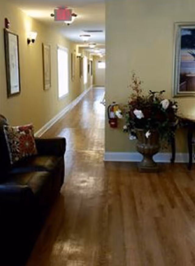 Long interior hallway with wood floors, a leather sofa and a floral arrangement next to a side table.
