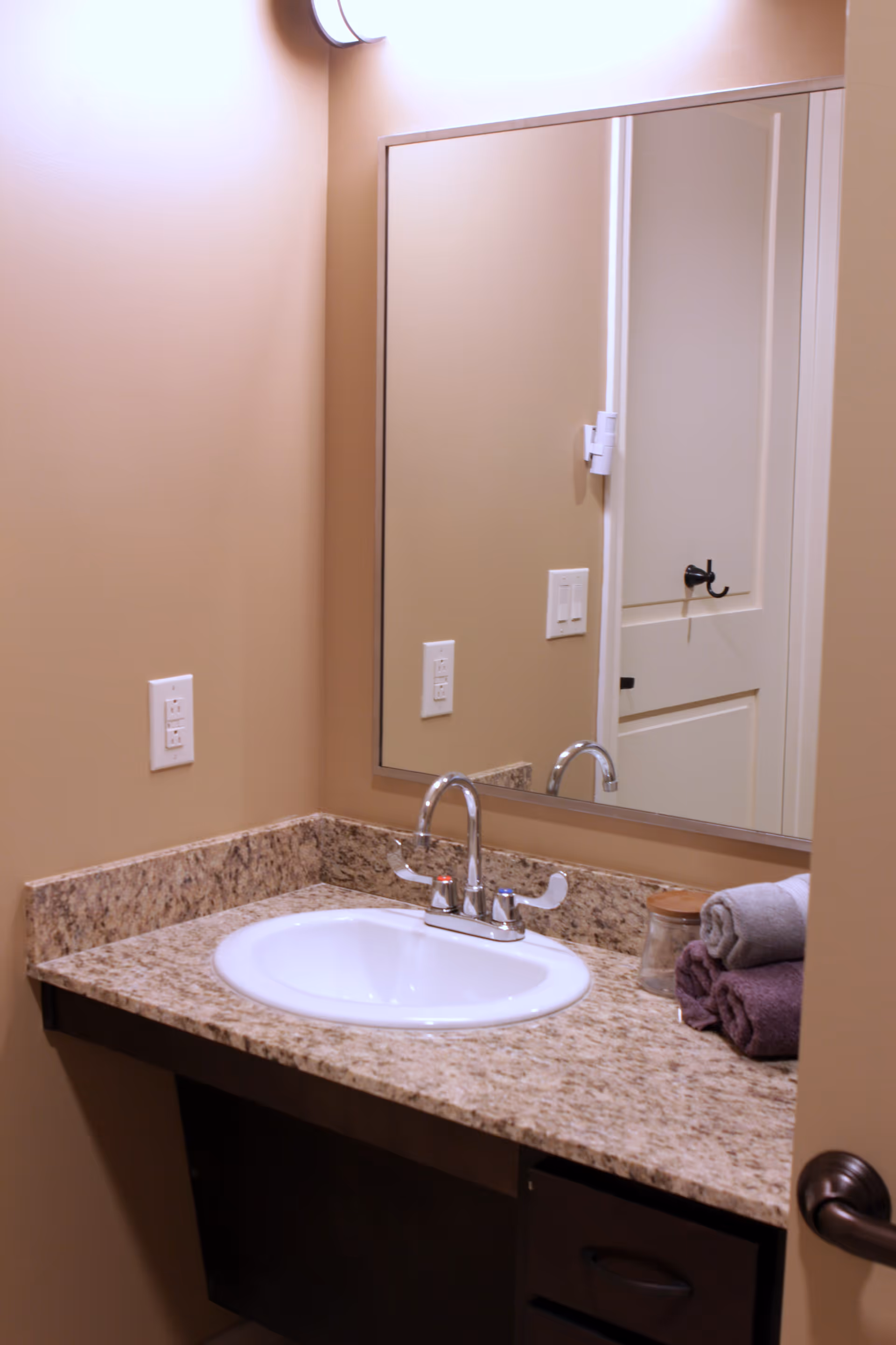 A bathroom vanity with a sink, chrome faucet, granite countertop, wall mirror, and folded towels.