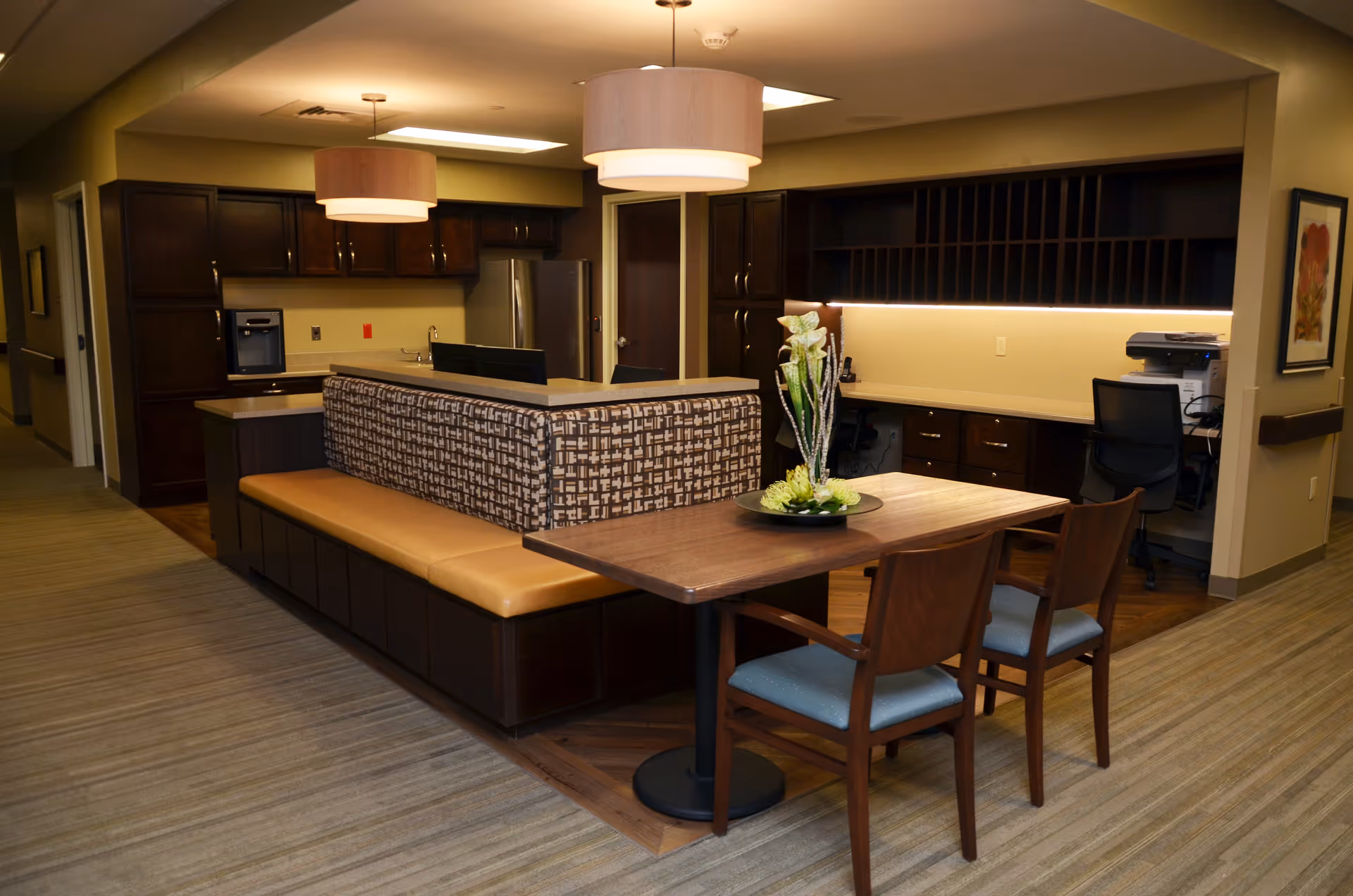 Interior common area with an upholstered bench, wooden table and chairs in front of a reception-style counter and built-in cabinetry.