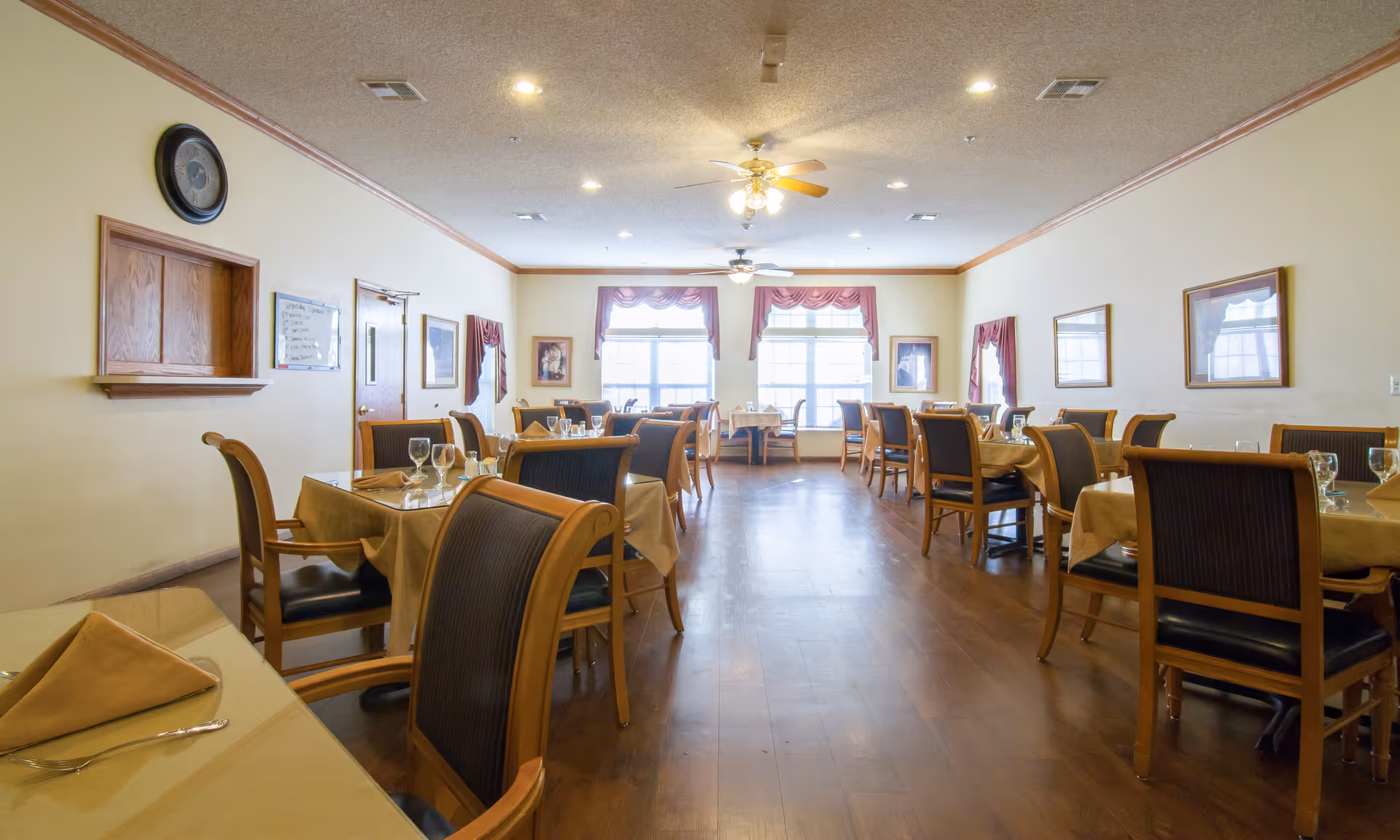 Bright, well-appointed dining room with multiple set tables and chairs and large windows at the far end.