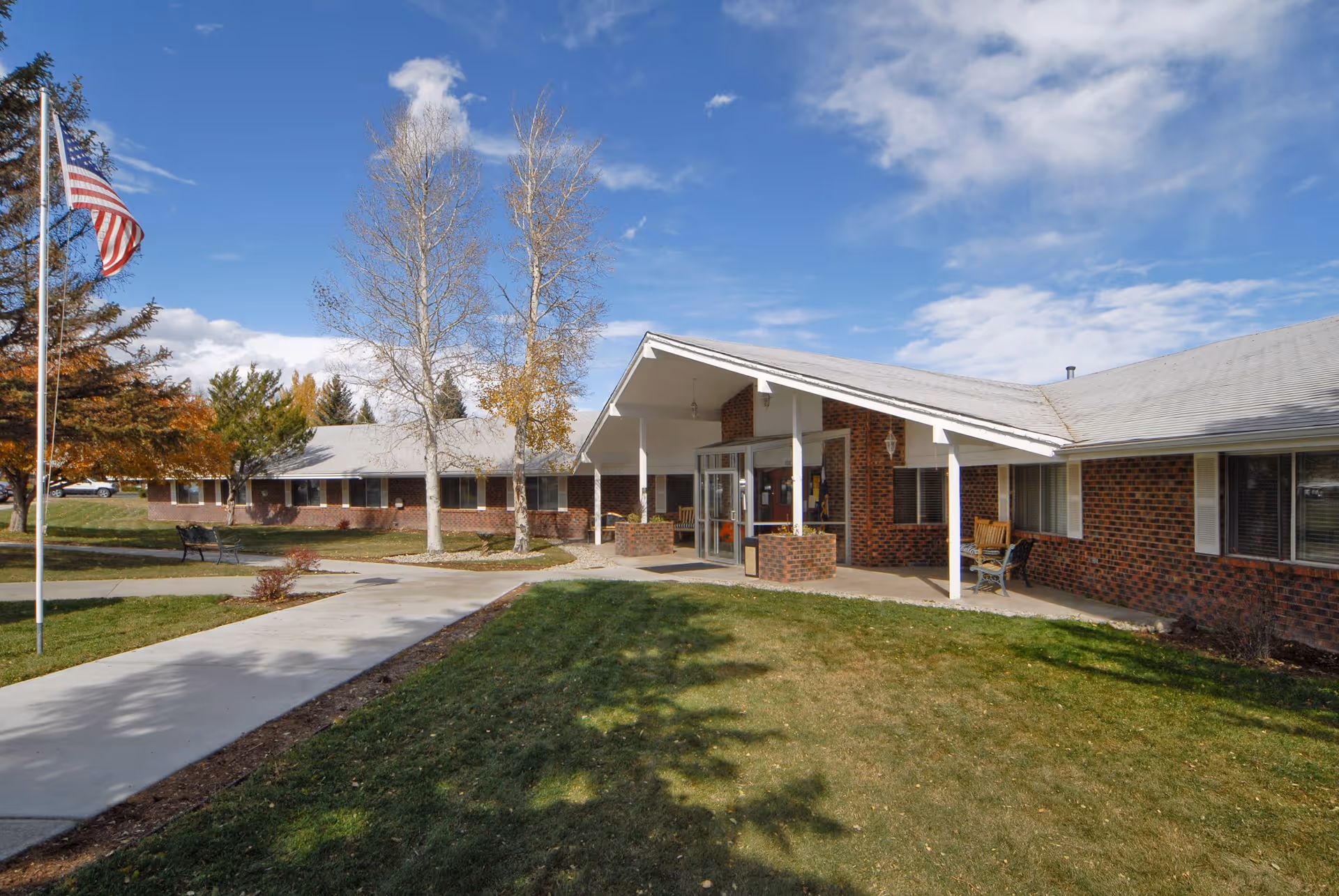 Front exterior of a single-story brick care center with a covered entrance, flagpole, walkway and lawn under a blue sky.