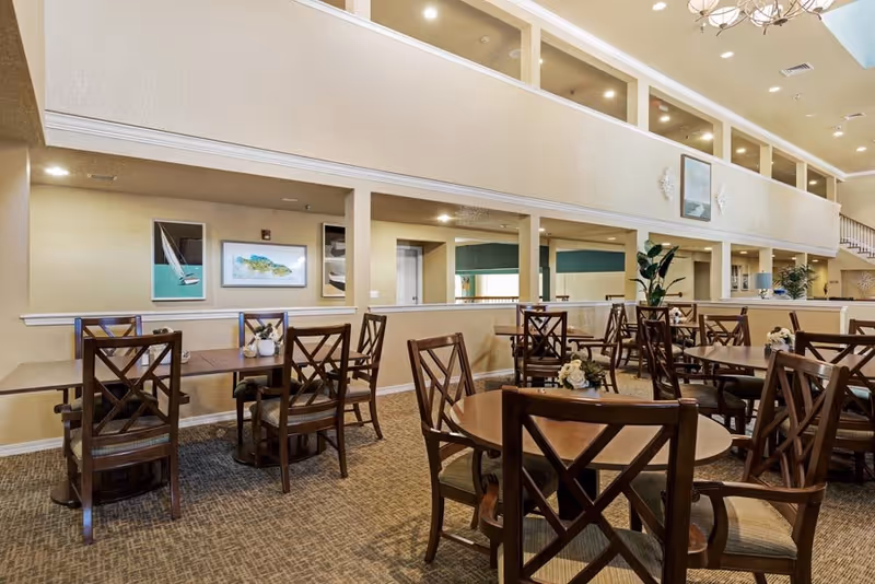 Spacious communal dining room with wooden tables and chairs arranged under a high ceiling.