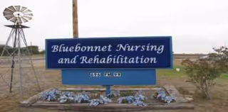 Bluebonnet Nursing and Rehabilitation sign on a rural exterior with a windmill and flowers.