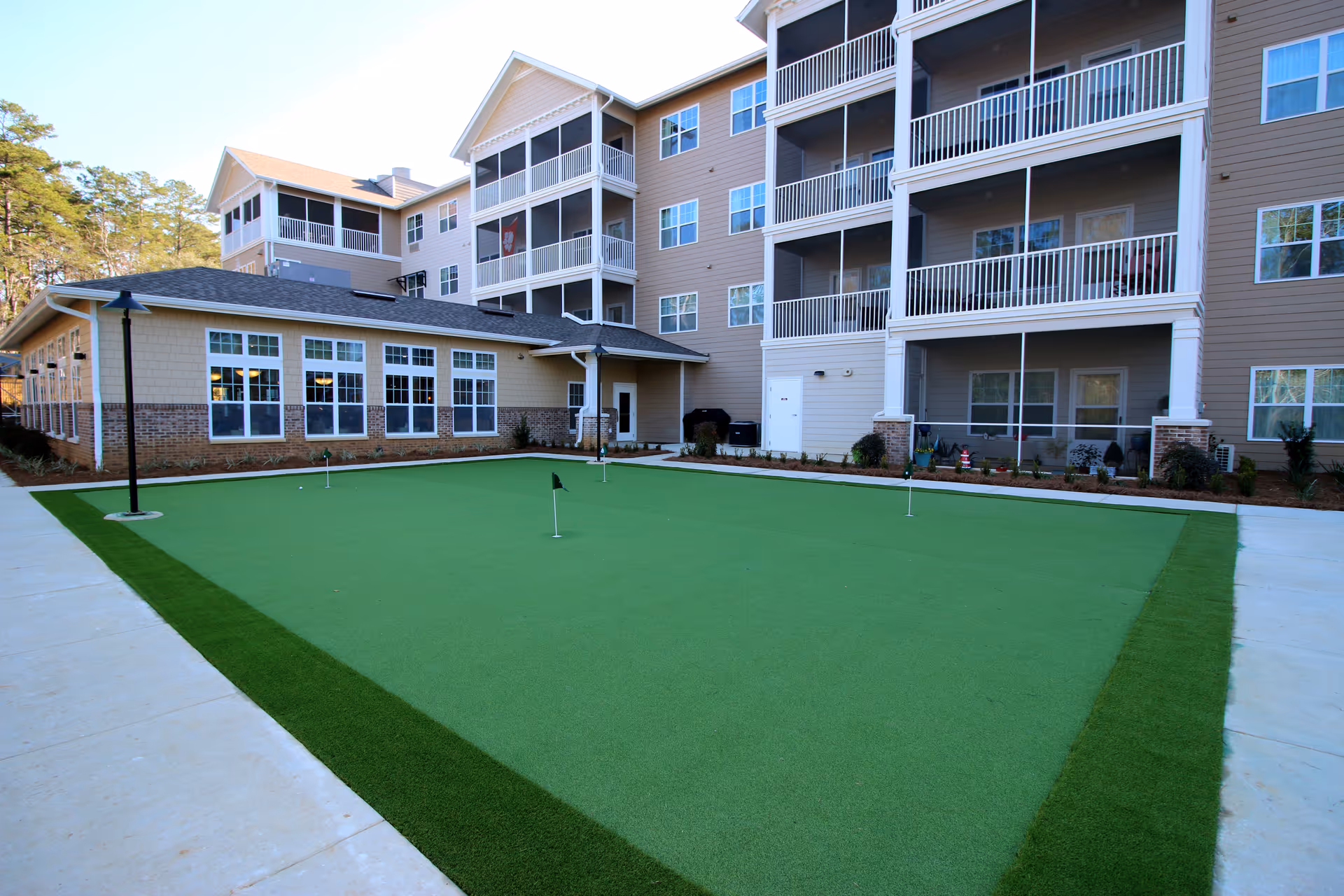 Multi-story senior living building exterior with a central putting green and covered balconies.