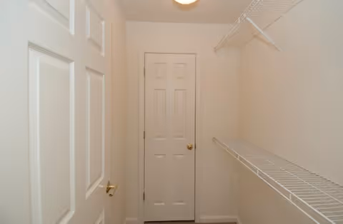 A small empty closet with white walls, two white doors with gold-colored handles, and white wire shelving on the right side.