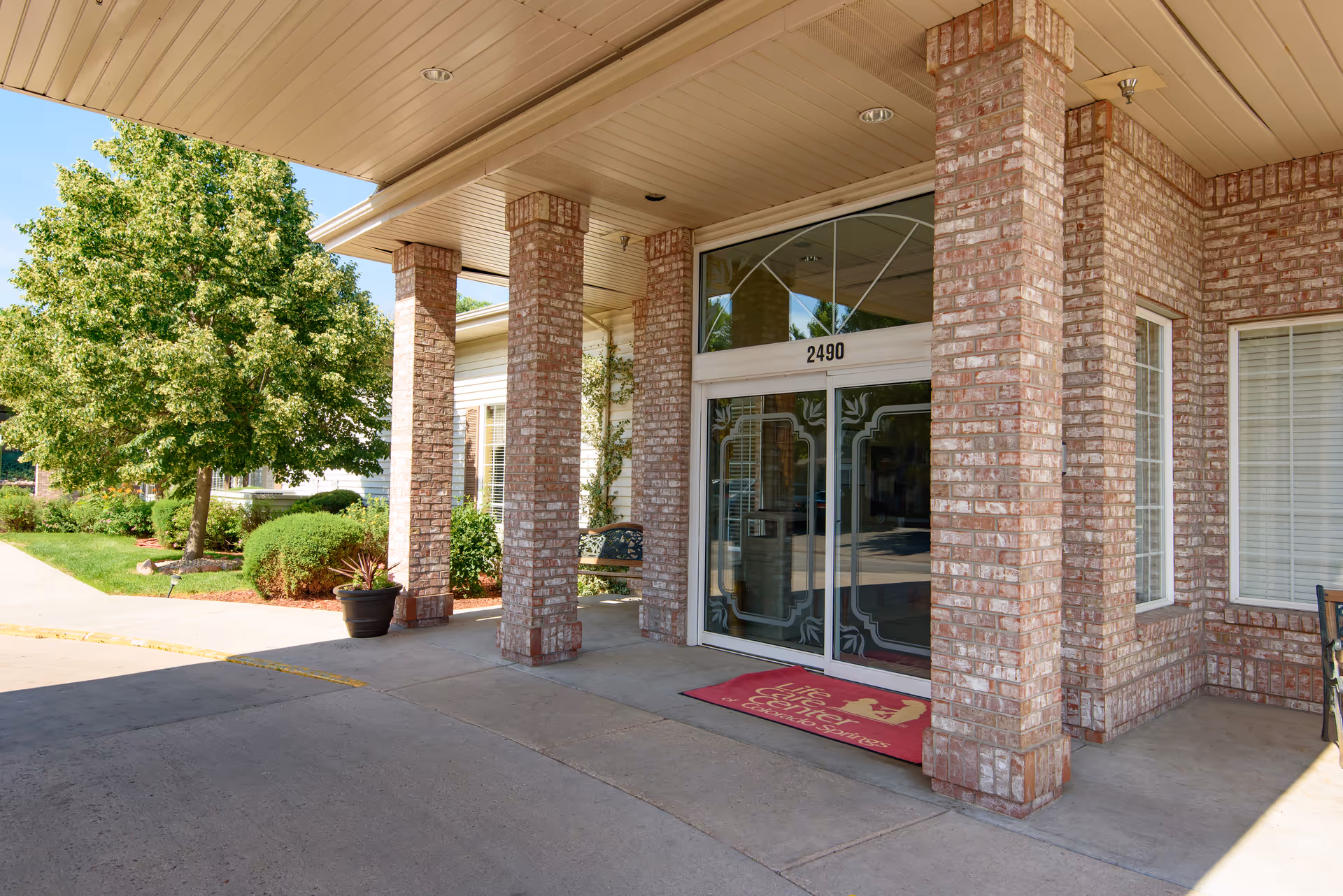 Covered brick entrance with columns and glass double doors under a portico, an address number above the doors and a red welcome mat.