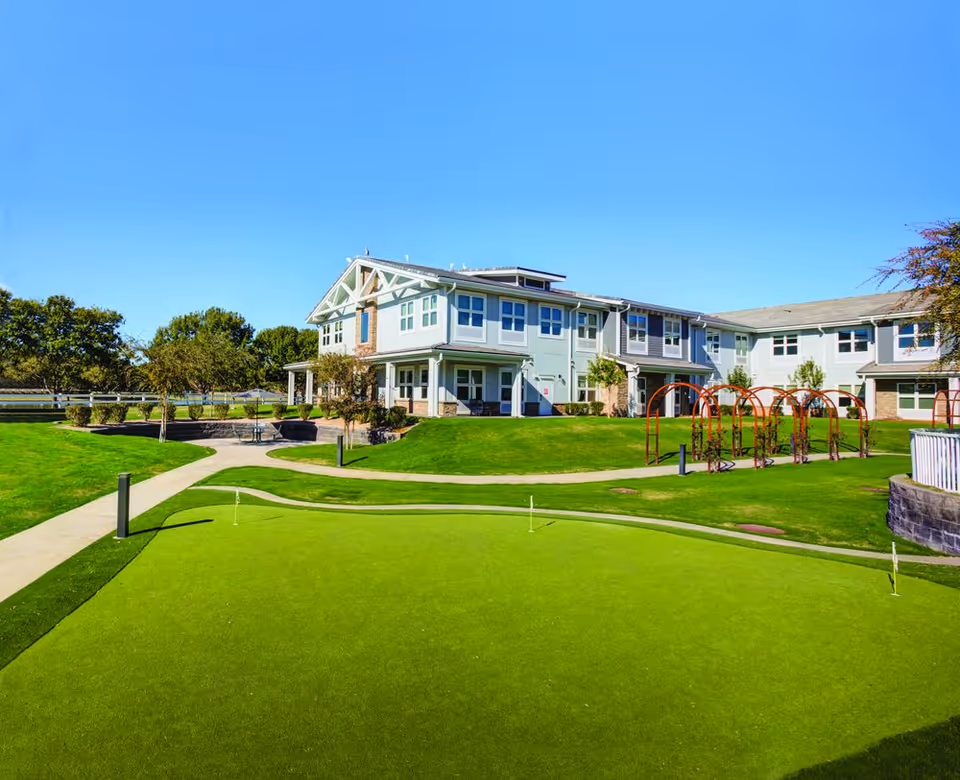 Exterior view of a senior living facility with green lawns, pathways, and playground structures.