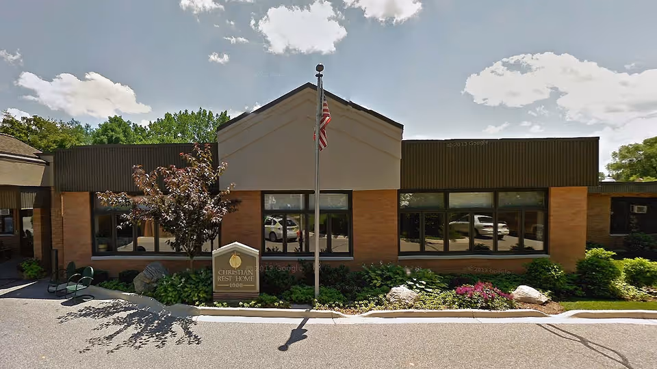 Front exterior of a single-story brick senior care building with an American flag and a sign reading "Christian Rest Home".