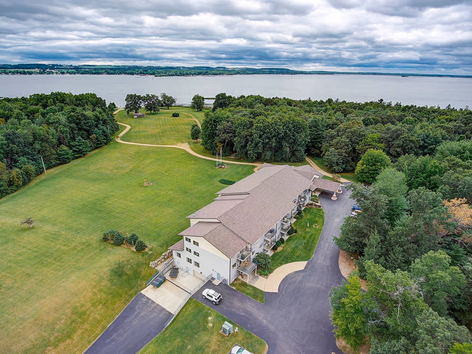 Aerial view of a senior living facility named MasonWoods surrounded by green lawns and trees, with a large body of water in the background under a cloudy sky.