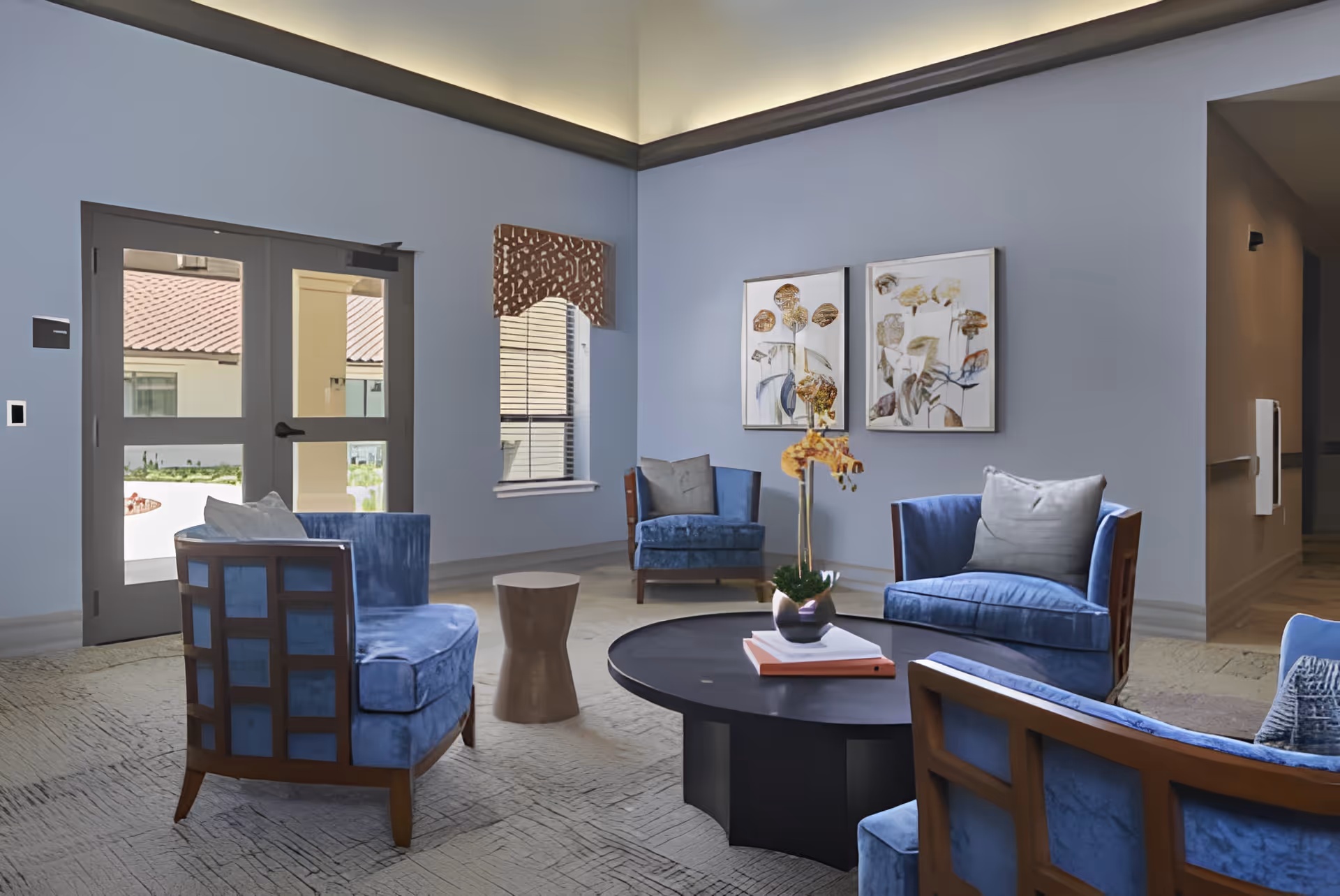 Communal seating area with blue upholstered chairs arranged around a round black coffee table in a softly lit lobby.