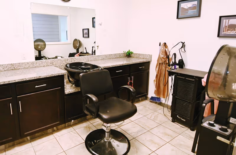 Salon chair and styling station with sink, mirrors, and hair equipment inside a facility.