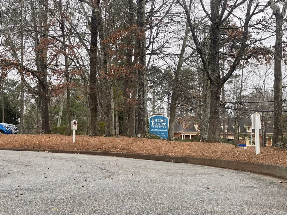 Driveway and parking area bordered by trees with an 'Arbor Terrace of Decatur' sign near the facility entrance.