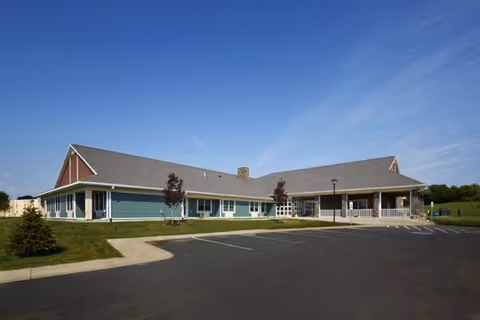 Front exterior of a retirement community building with a parking lot and clear blue sky.