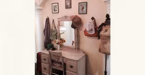 A vintage vanity with mirror, hats, and a dress form in a cozy interior.