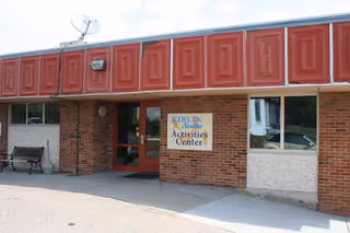 Front entrance of a single-story brick building with red trim and a sign that reads 'Activities Center'.