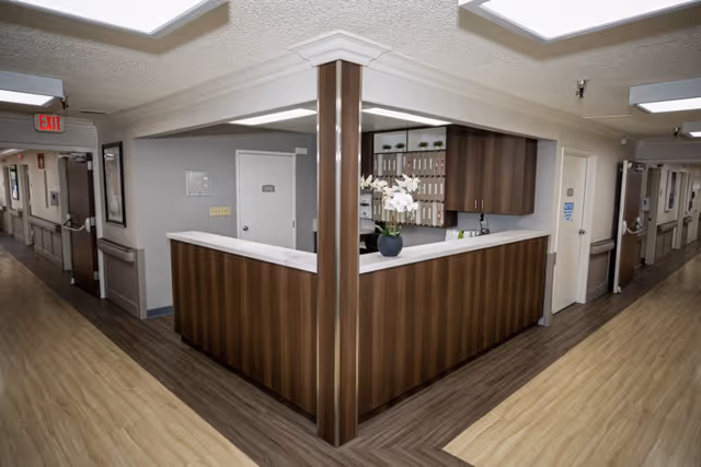 Wood-paneled reception/nurse station at the junction of two hallways inside a senior living facility.