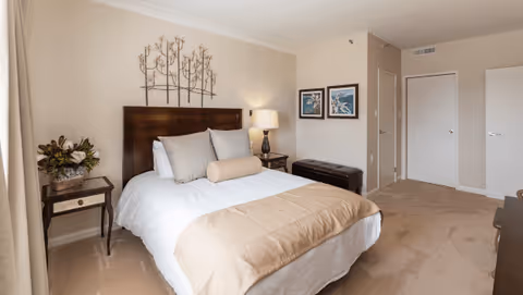 Neat bedroom with a made double bed, headboard, bedside tables with lamp and decor, wall art, and closet doors.