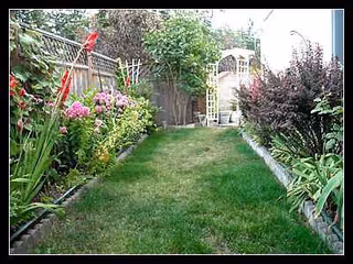 Narrow grassy path bordered by flowering beds and a lattice arch at the end.