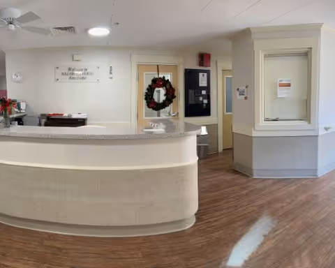 Interior reception desk and lobby of a senior living facility with a curved counter and a holiday wreath on a door behind the desk.
