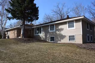 Exterior view of a single-story beige building with trees and a grassy yard.