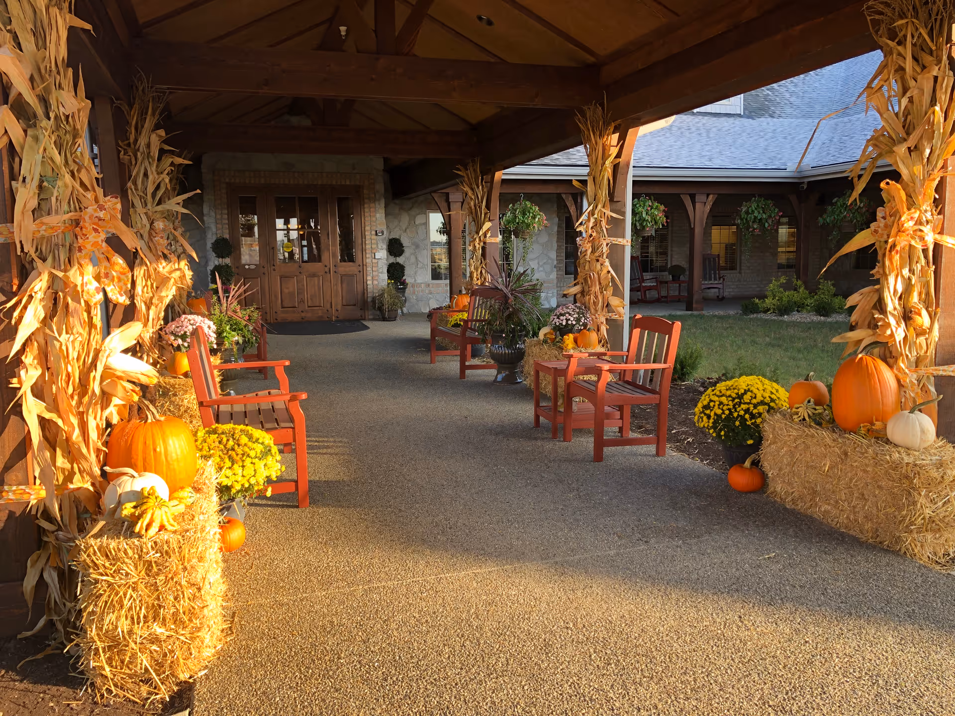 Covered entrance walkway decorated with pumpkins, hay bales, cornstalks and red benches.